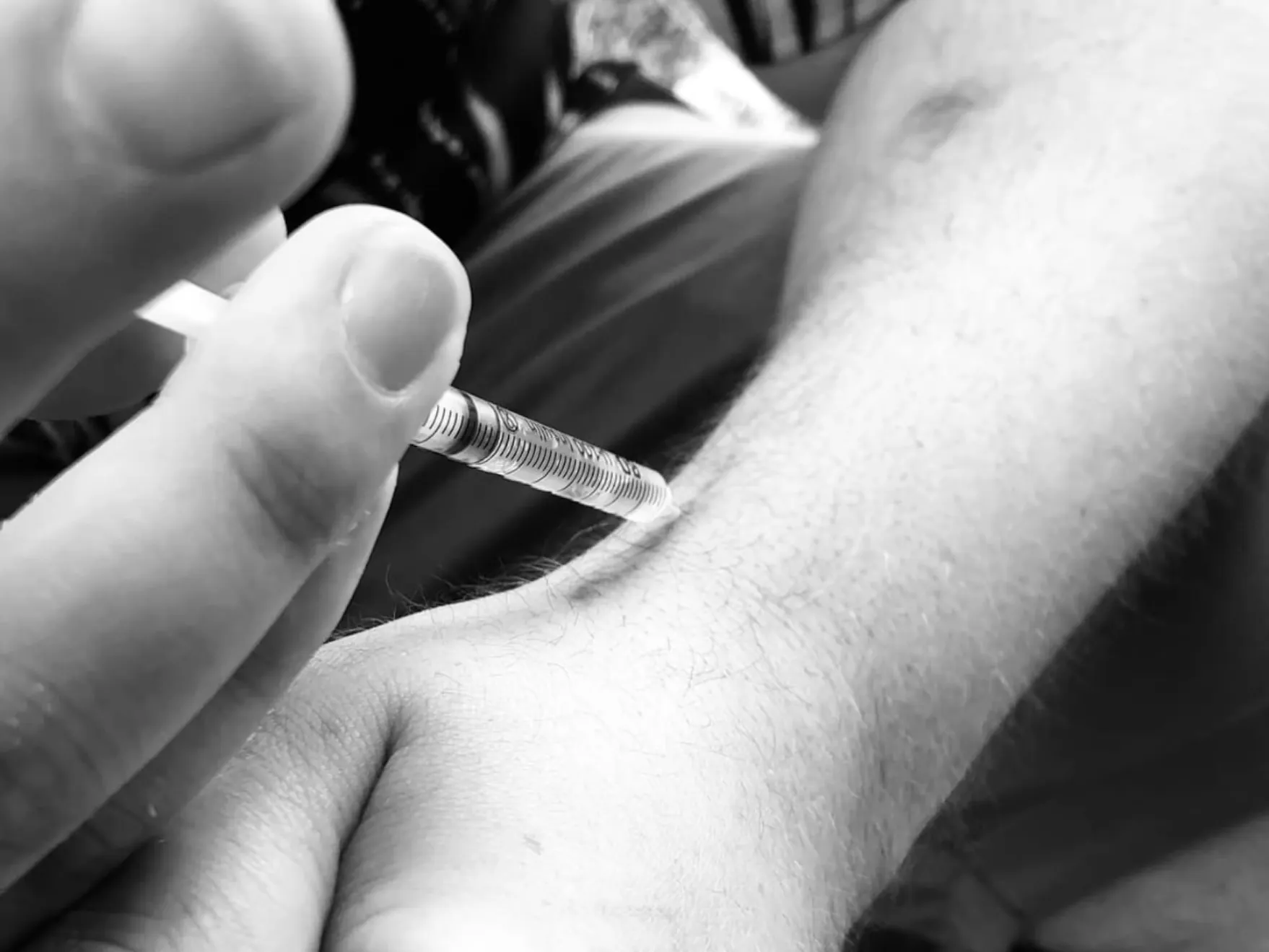 Detajl moške roke, medtem ko si z injekcijo vbrizgava mamilo v žilo.